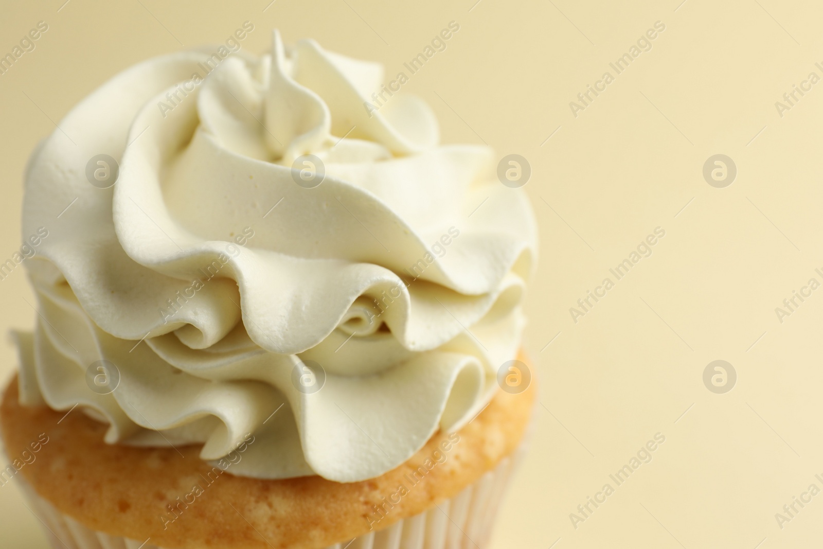 Photo of Tasty vanilla cupcake with cream on pale yellow background, closeup. Space for text