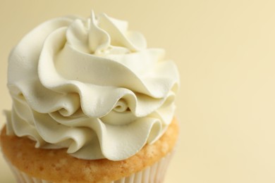 Tasty vanilla cupcake with cream on pale yellow background, closeup. Space for text