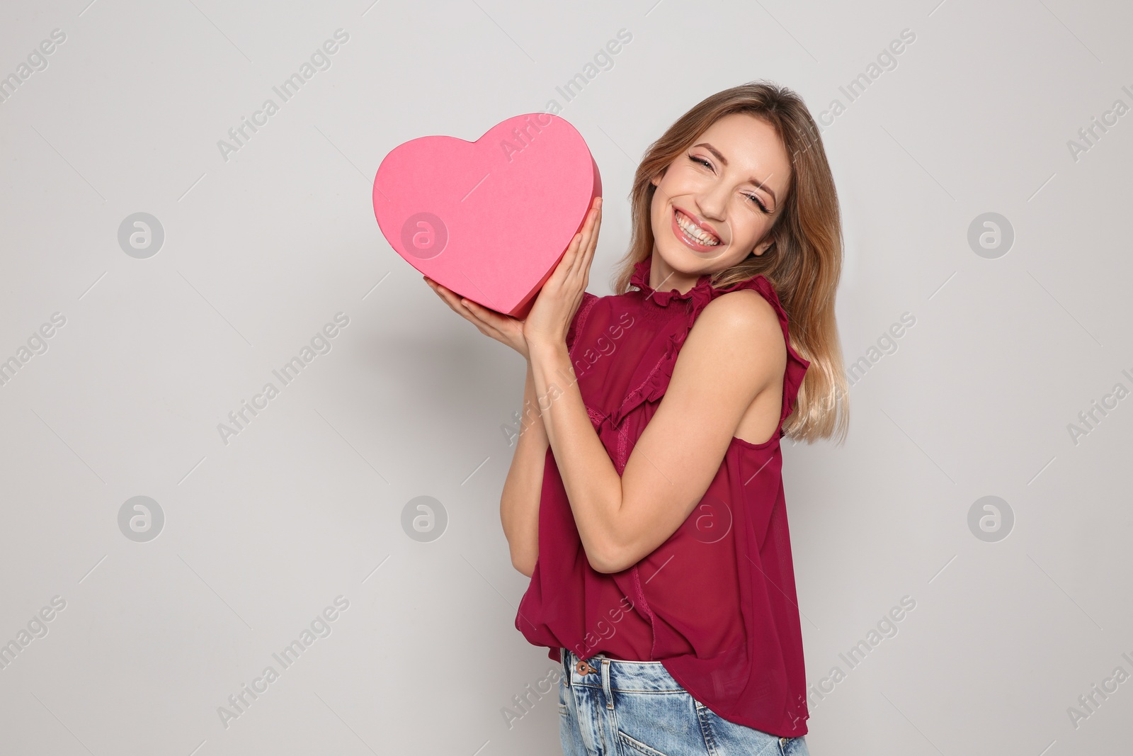 Photo of Portrait of beautiful smiling girl with heart shaped gift box on light background. International Women's Day