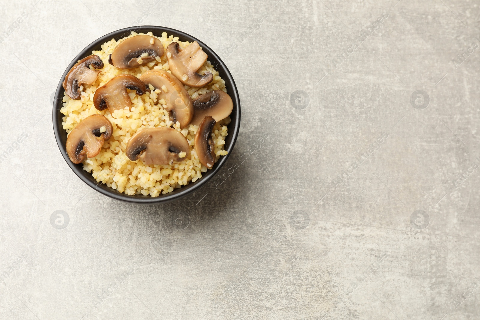 Photo of Delicious bulgur with mushrooms in bowl on gray table, top view. Space for text