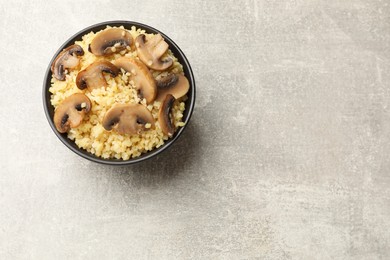 Photo of Delicious bulgur with mushrooms in bowl on gray table, top view. Space for text