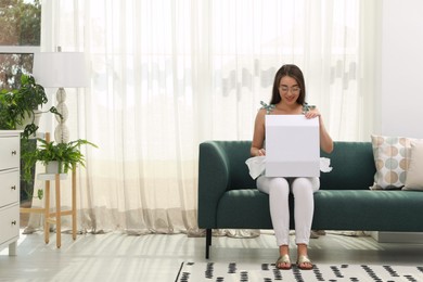 Photo of Happy young woman opening parcel at home. Internet shopping