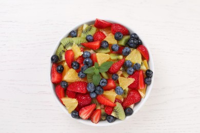 Photo of Delicious fresh fruit salad in bowl on white wooden table, top view