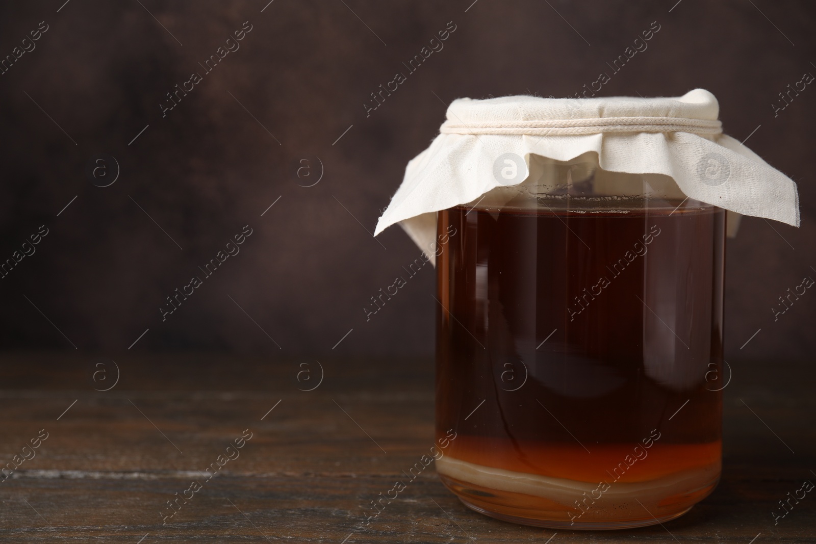 Photo of Tasty kombucha in glass jar on wooden table, space for text