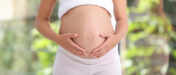 Pregnant woman on blurred green background, closeup. Banner design