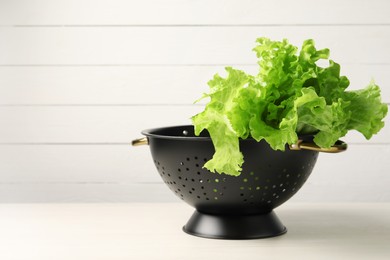 Fresh lettuce in black colander on white wooden table. Space for text