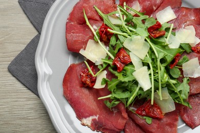 Photo of Plate of tasty bresaola salad with sun-dried tomatoes and parmesan cheese on wooden table, top view