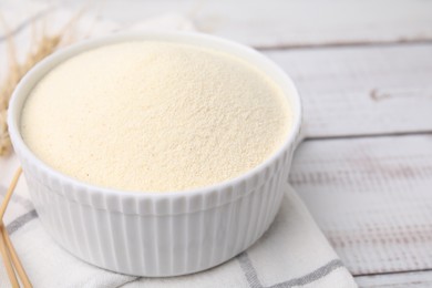 Photo of Uncooked organic semolina in bowl on white wooden table, closeup. Space for text