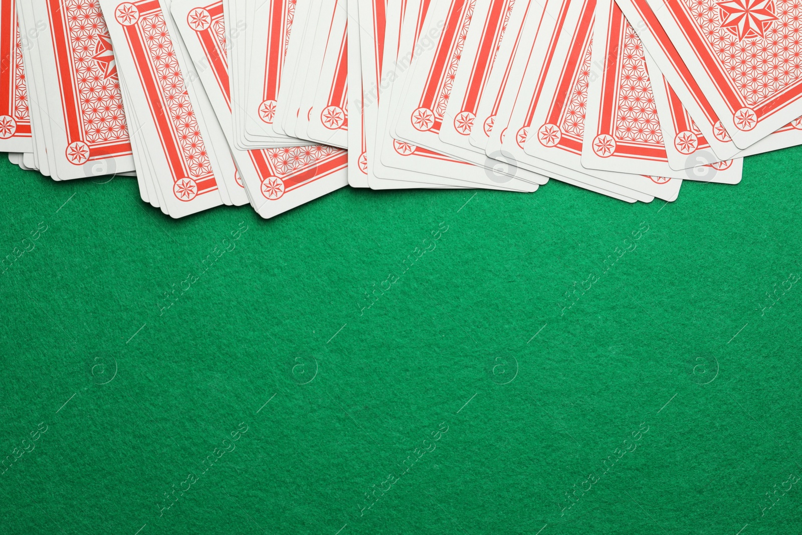 Photo of Deck of playing cards on green table, top view. Space for text