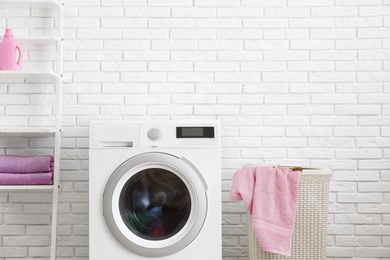 Modern washing machine near brick wall in laundry room interior