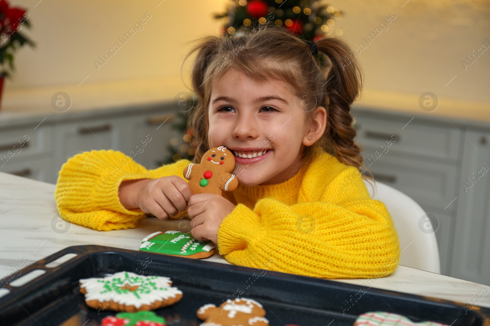 Photo of Cute little girl with freshly baked Christmas gingerbread cookies at table indoors