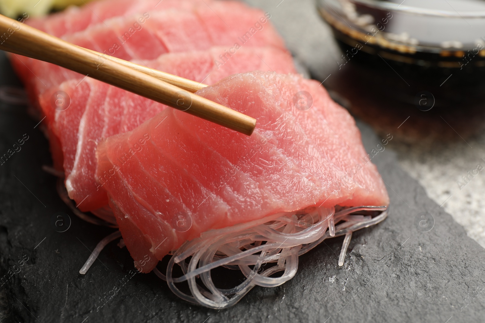 Photo of Taking tasty sashimi (pieces of fresh raw tuna) from black board, closeup