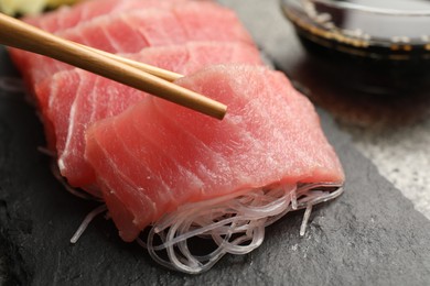 Photo of Taking tasty sashimi (pieces of fresh raw tuna) from black board, closeup
