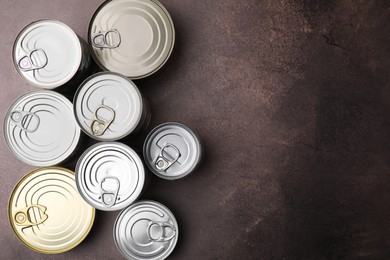 Photo of Many closed tin cans on brown table, flat lay. Space for text