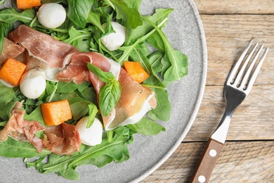 Photo of Fresh melon with prosciutto, mozzarella and arugula on wooden table, closeup