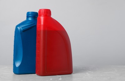 Photo of Motor oil in different canisters on grey marble table against light background, space for text