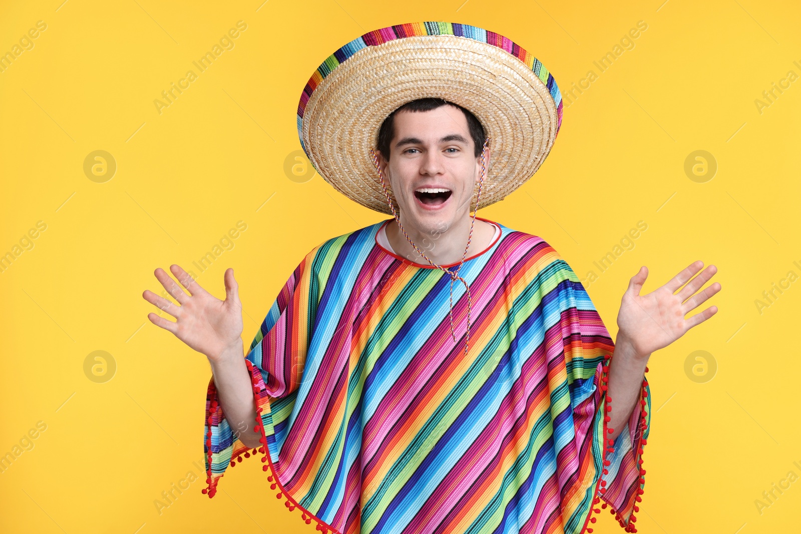 Photo of Excited man in Mexican sombrero hat and poncho on yellow background