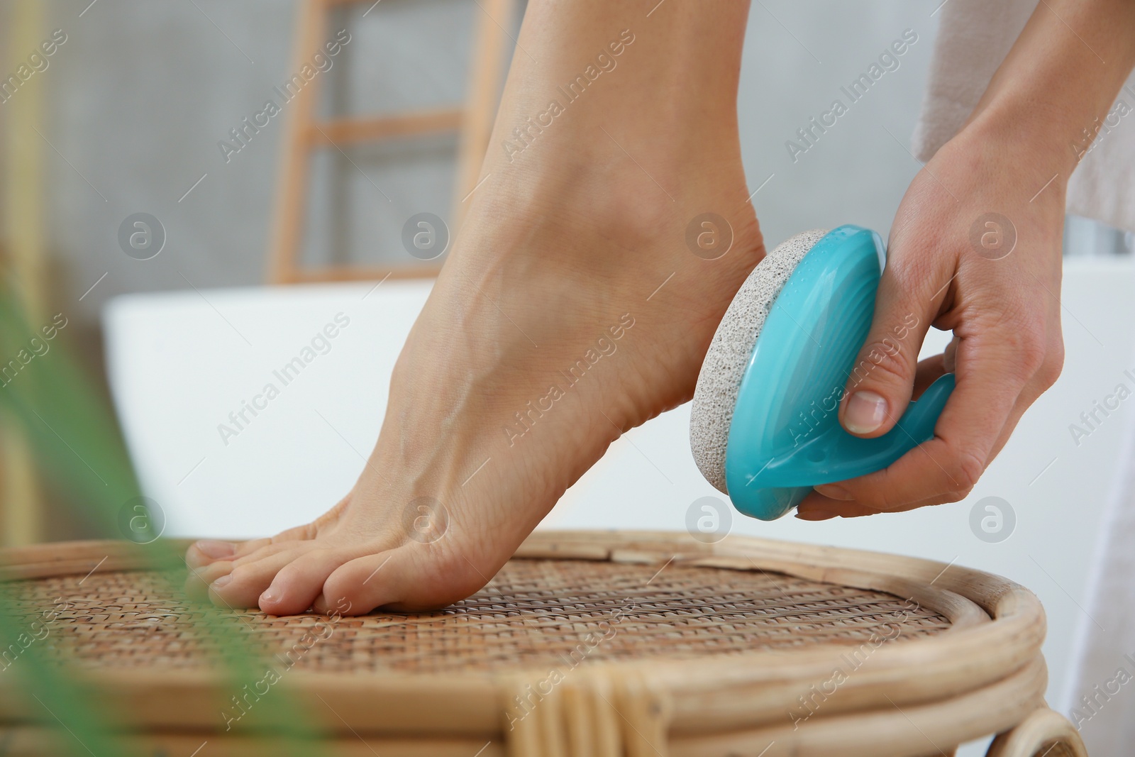 Photo of Woman using pumice stone for removing dead skin from feet in bathroom, closeup