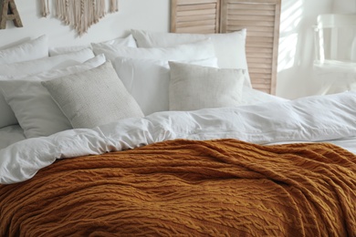 Photo of Warm orange knitted plaid on bed indoors