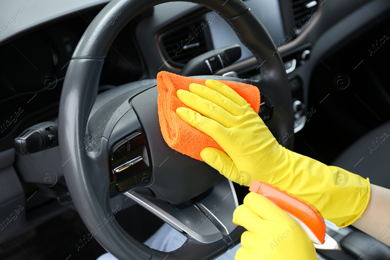 Photo of Woman cleaning steering wheel with rag in car, closeup