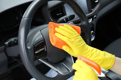 Photo of Woman cleaning steering wheel with rag in car, closeup
