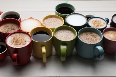 Many different cups with aromatic hot coffee on white wooden table