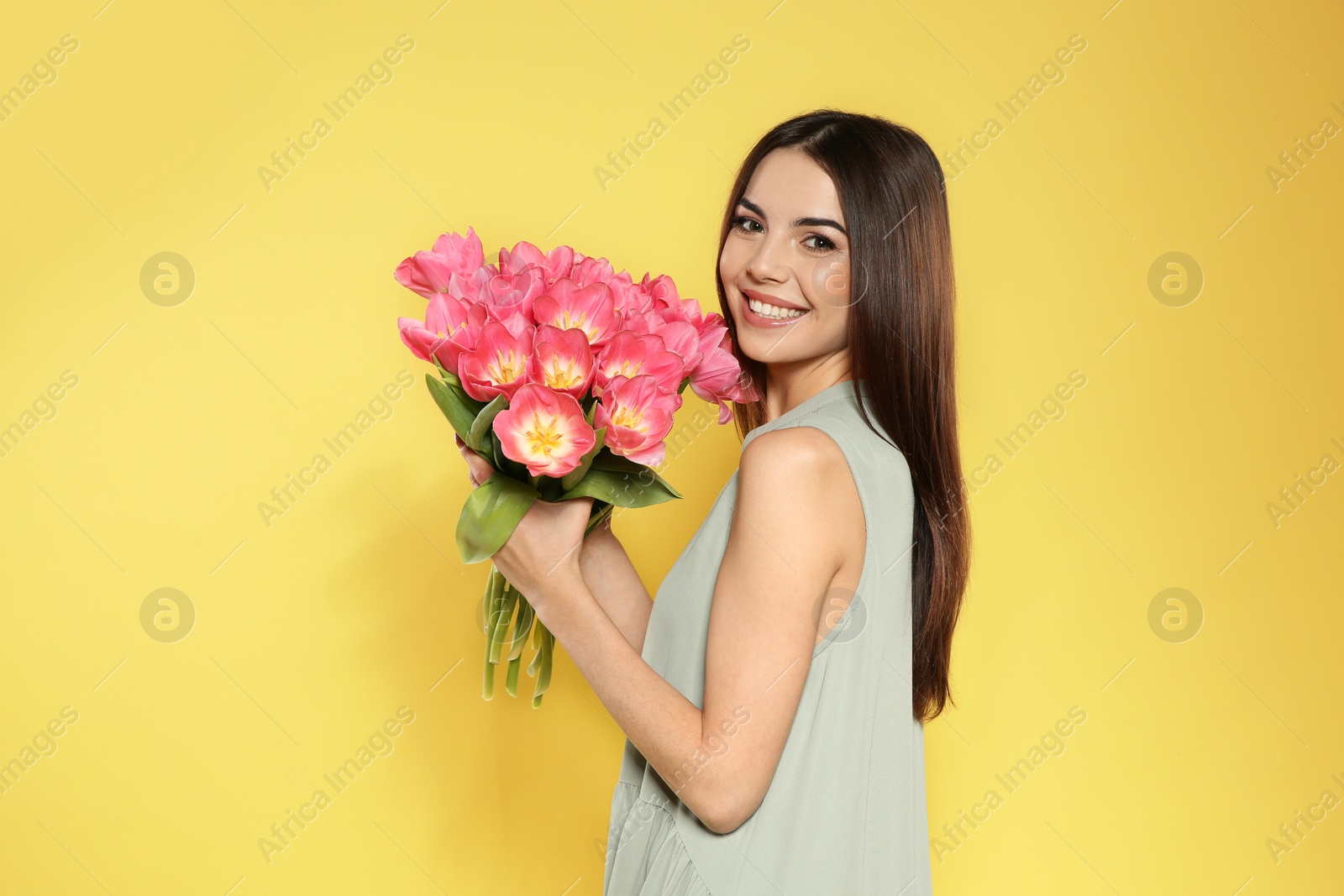 Photo of Portrait of beautiful smiling girl with spring tulips on yellow background. International Women's Day