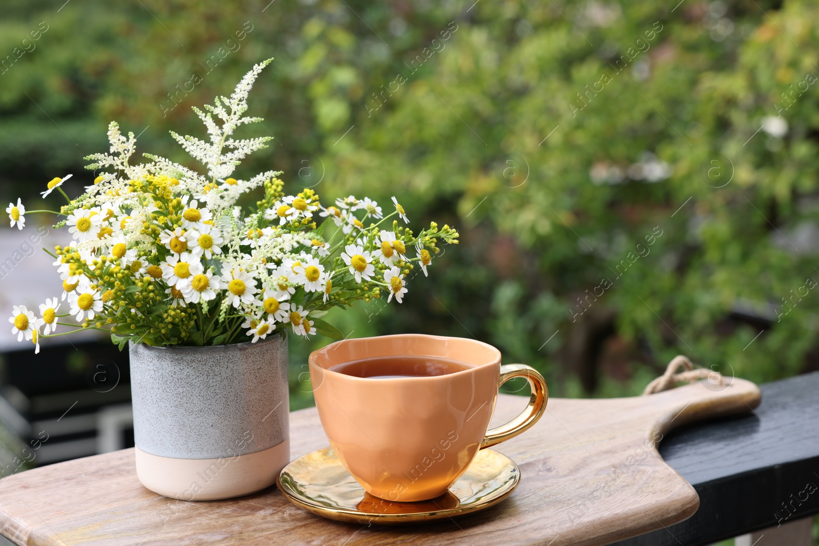 Photo of Cup of delicious chamomile tea and fresh flowers outdoors. Space for text