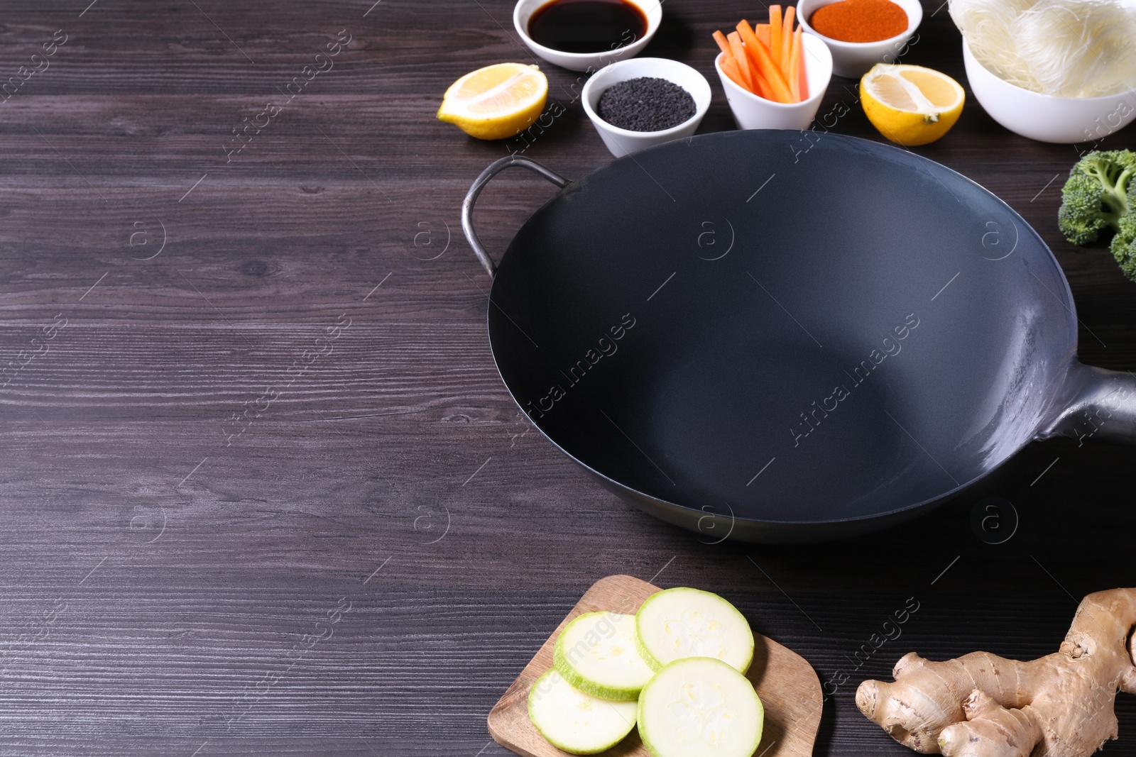 Photo of Empty iron wok and ingredients on grey wooden table. Space for text