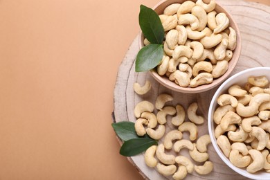 Photo of Tasty cashew nuts and green leaves on pale brown background, top view. Space for text