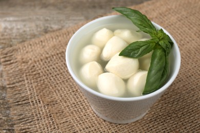 Photo of Tasty mozzarella balls and basil leaves in bowl on wooden table