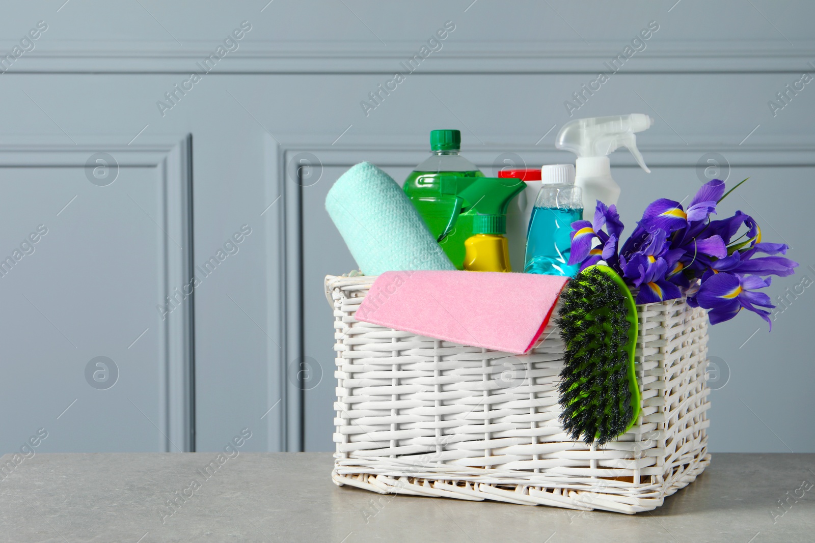 Photo of Spring cleaning. Basket with detergents, flowers and tools on grey textured table. Space for text