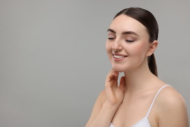 Photo of Smiling woman touching her neck on grey background. Space for text