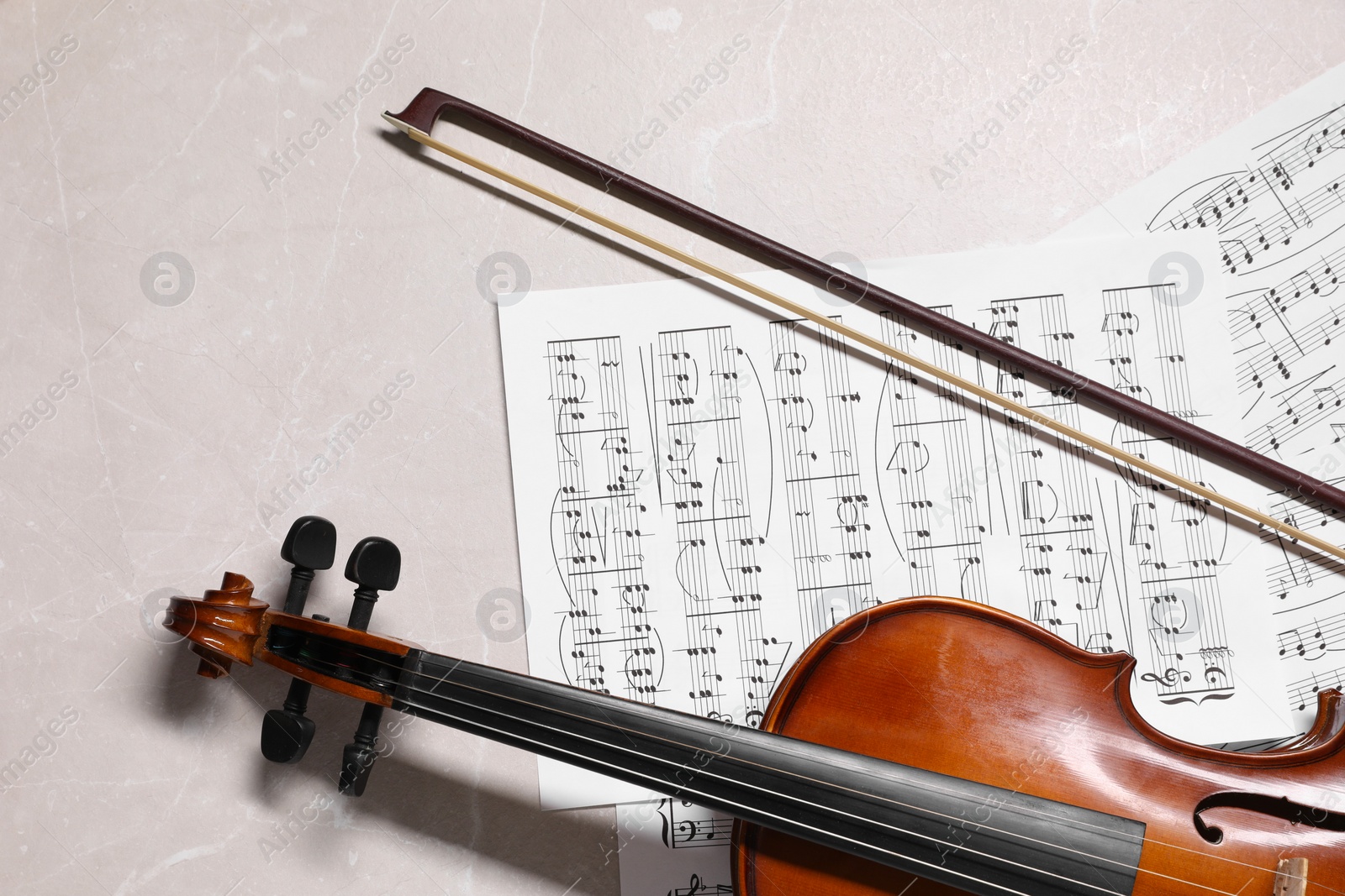 Photo of Violin, bow and music sheets on grey marble table, top view