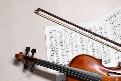 Violin, bow and music sheets on grey marble table, top view