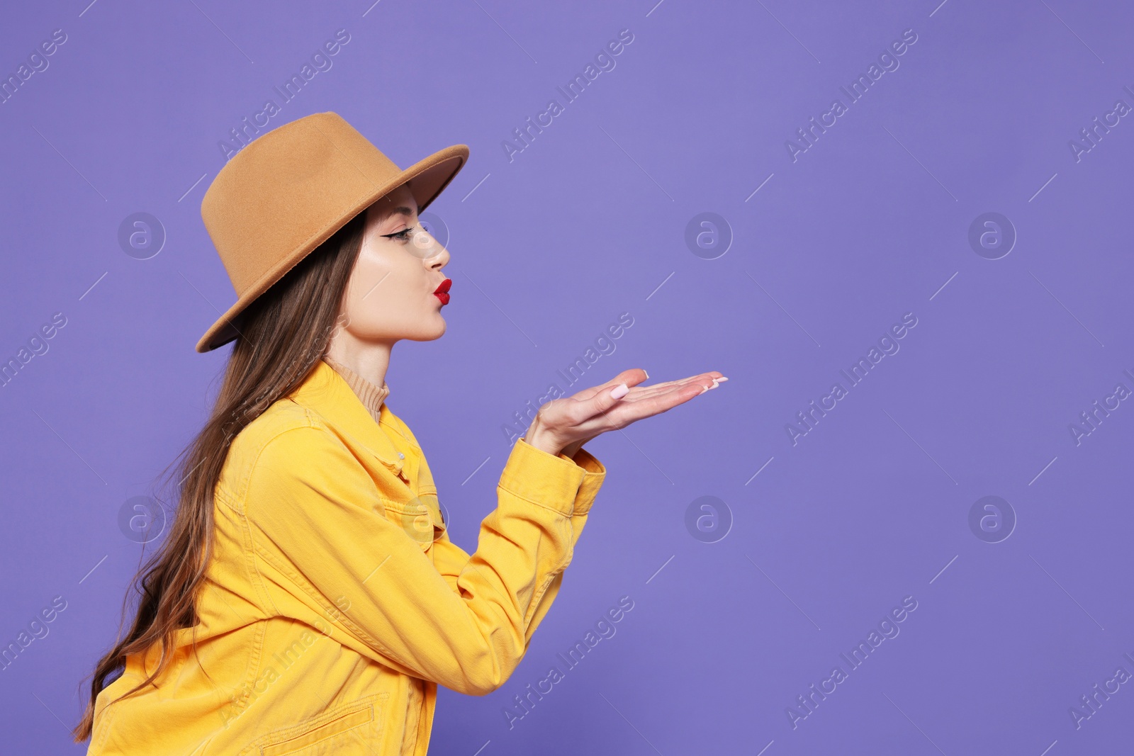 Photo of Beautiful young woman blowing kiss on purple background, space for text