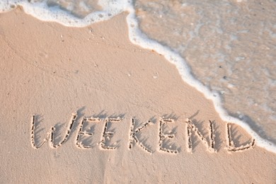 Word Weekend written on sand at beach, above view