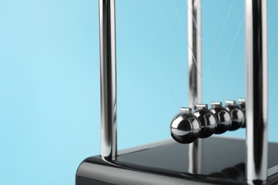 Photo of Newton's cradle on light blue background, closeup. Physics law of energy conservation