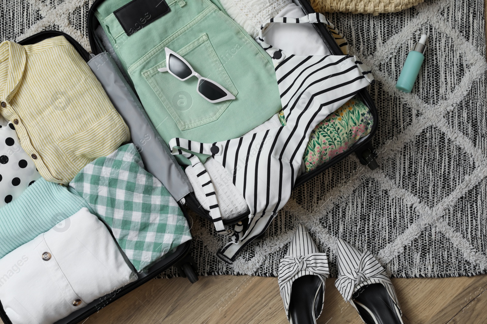 Photo of Open suitcase with summer clothes, accessories and shoes on floor, flat lay