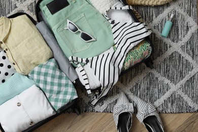 Open suitcase with summer clothes, accessories and shoes on floor, flat lay