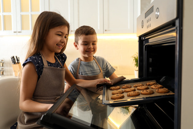 Cute little children taking cookies out of oven in kitchen. Cooking pastry