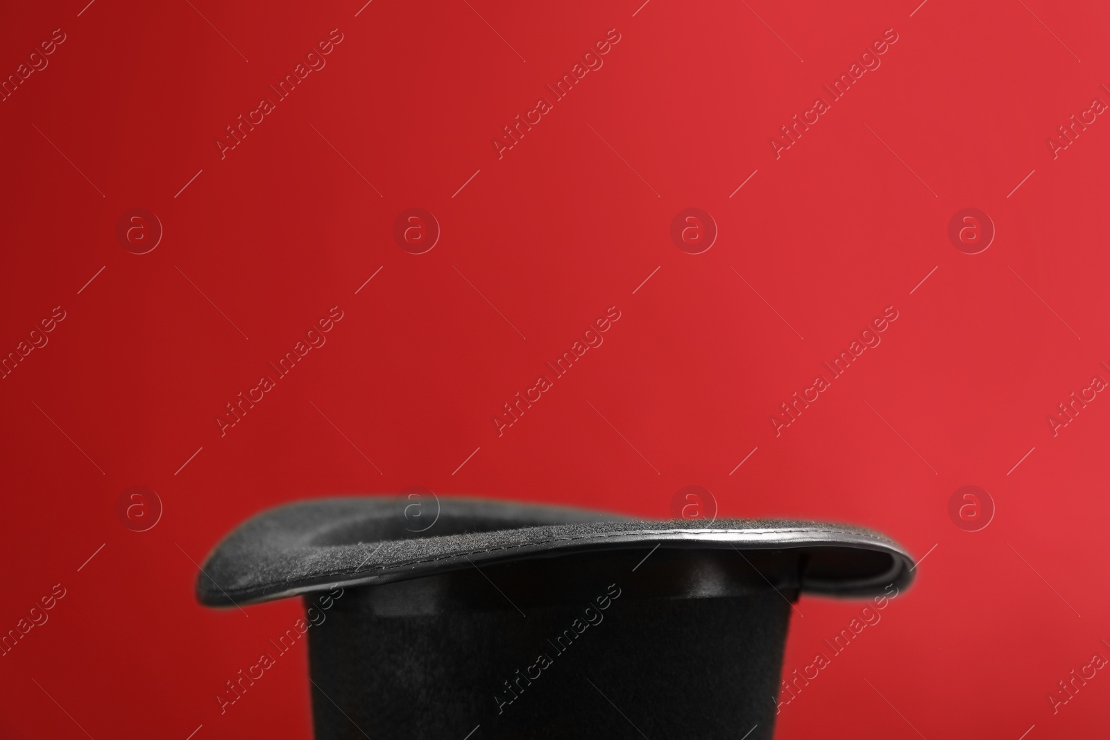 Photo of Black magician's hat on red background, closeup. Space for text