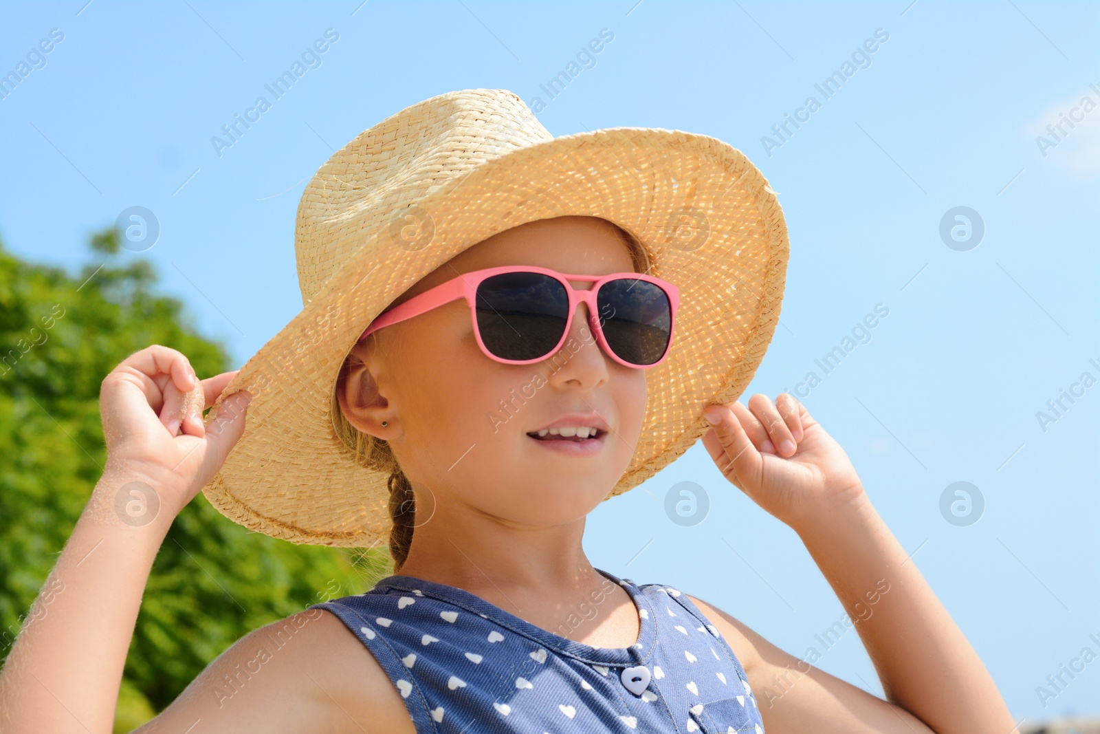 Photo of Little girl wearing sunglasses and hat at beach on sunny day