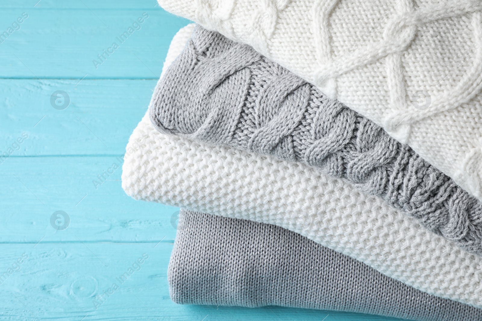 Image of Stack of folded warm sweaters on turquoise wooden background, closeup