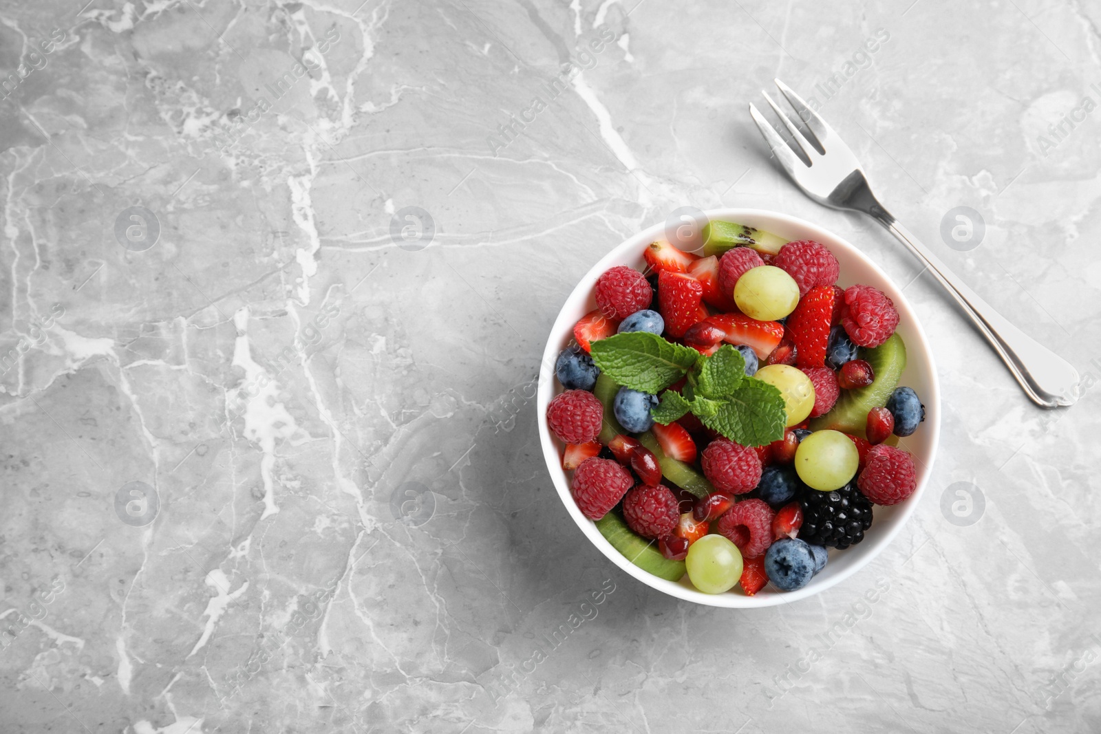 Photo of Fresh fruit salad on grey marble table, flat lay. Space for text