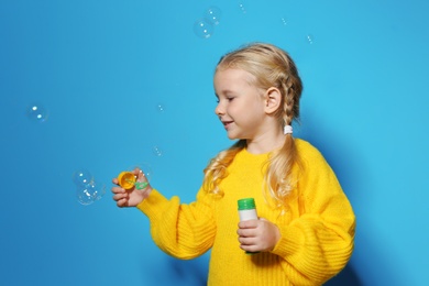 Cute little girl blowing soap bubbles on color background