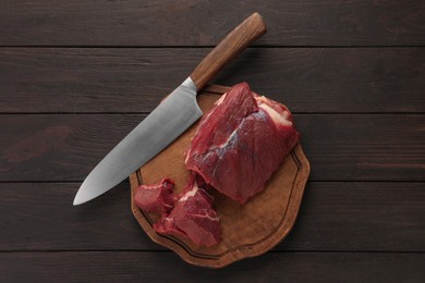 Photo of Pieces of raw beef meat and knife on wooden table, top view