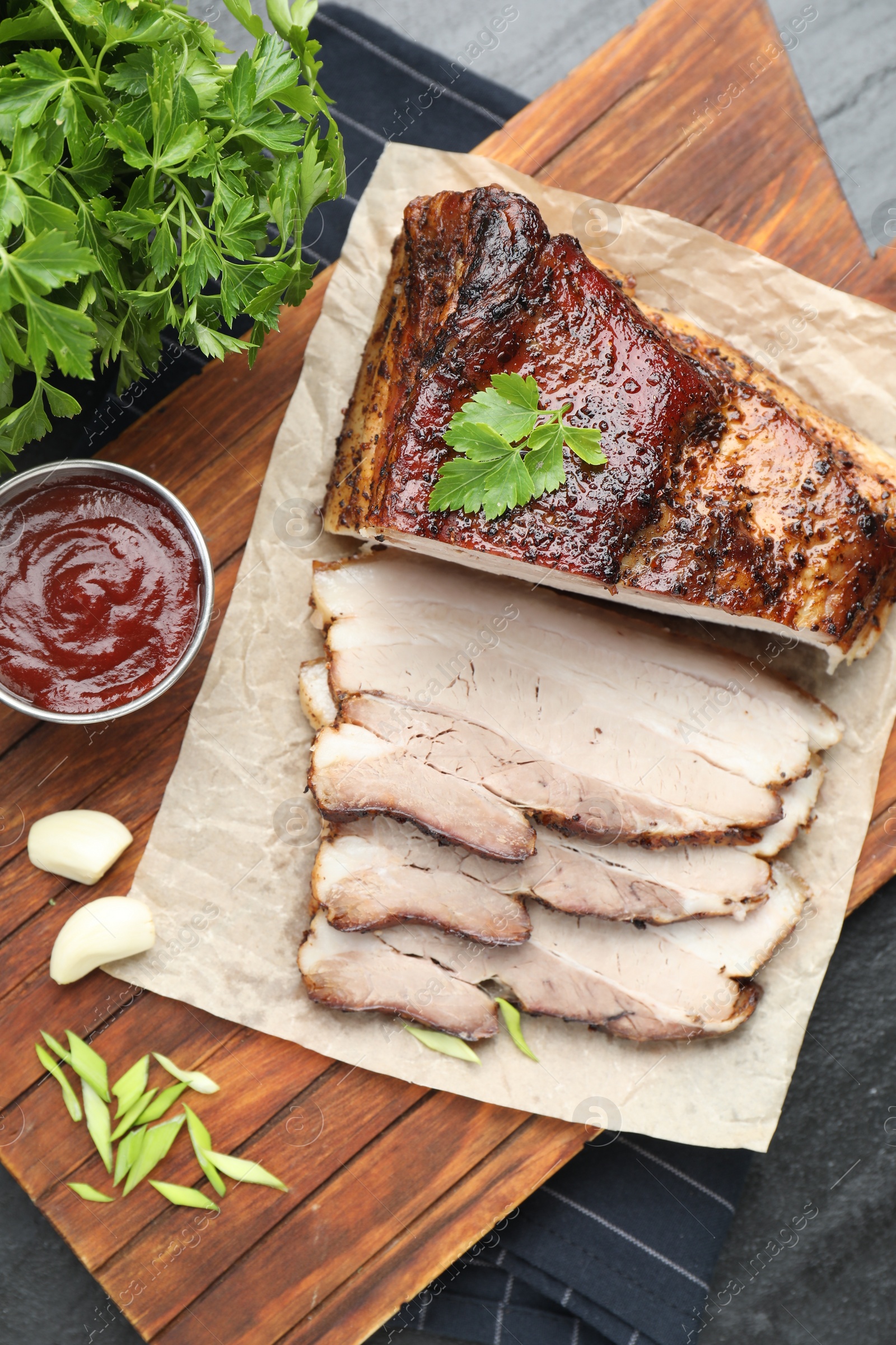 Photo of Pieces of baked pork belly served with sauce and parsley on black textured table, top view