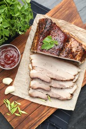 Photo of Pieces of baked pork belly served with sauce and parsley on black textured table, top view