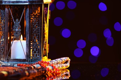 Photo of Arabic lantern, misbaha and folded prayer mat on mirror surface against blurred lights at night. Space for text